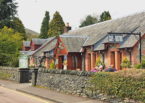 Photo of The Village Rest, Cafe and Bistro building in Luss, taken from the roadside at the front, with Leylandii trees peering over the top in the background